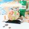 The bottom of an orange and yellow print water bottle bag is displayed with money, cell phone and chap stick. Beside the bag is a Stanley.
